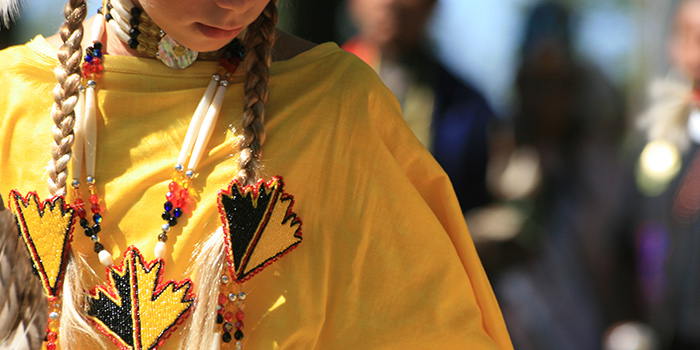 A young girl wearing traditional Native American dress looks at the ground