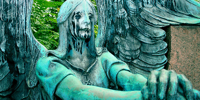 Oxidized copper statue of an angel that appears to be weeping