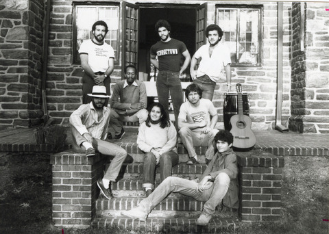 Black-and-white photograph of eight students standing and sitting on the brick steps outside of a house. steps outside 