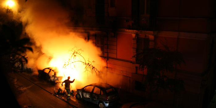 a person runs down a dark street while a car burns in the night