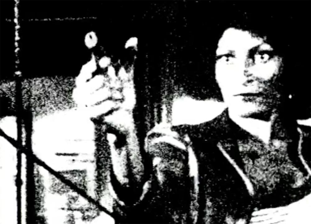 Grainy film still of a woman holding a gun