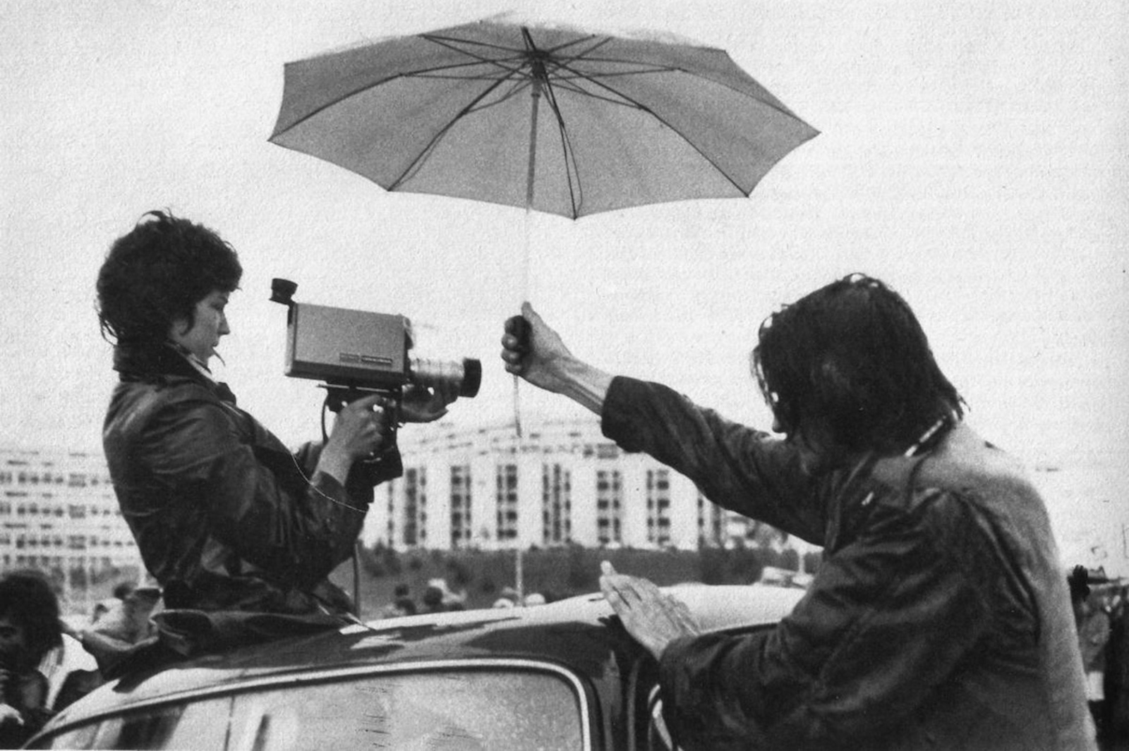 a woman filming through the sunroof of a car while someone holds an umbrella over them