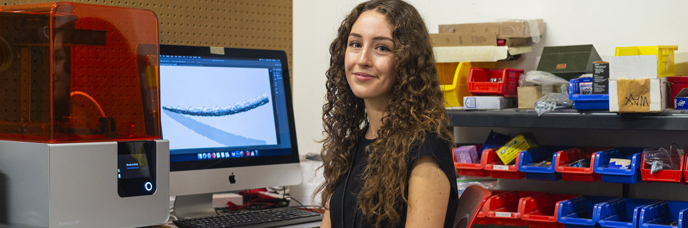 a student sits at a computer with product renderings visible on the screen