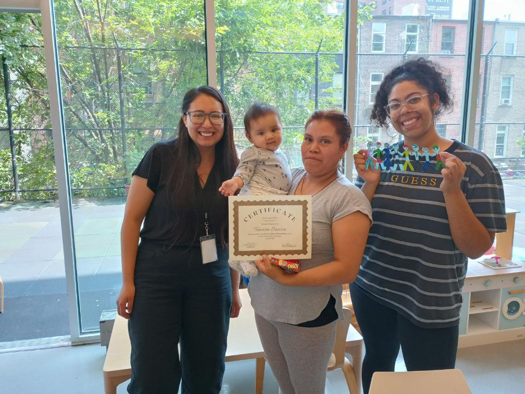 Jalexie Urena ’25 smiling with a certificate and a family at LSA Family Health Service in East Harlem, NY