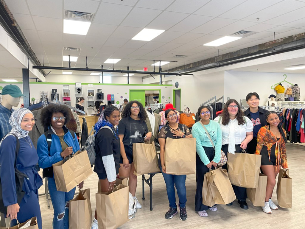 Students smiling and holding bags of clothing at The Wardrobe