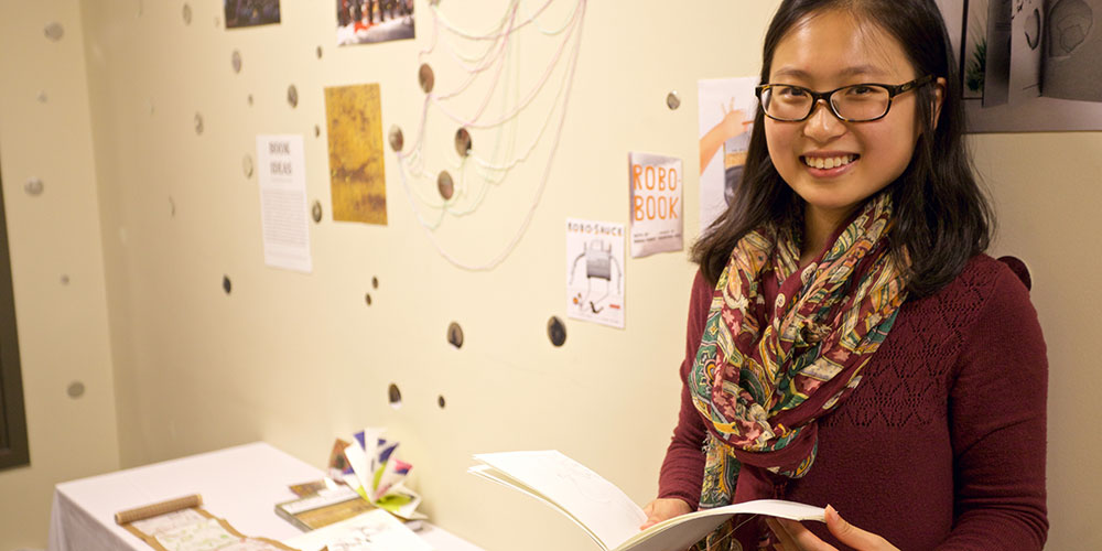 Honglan Huang holds a book in front of her exhibition