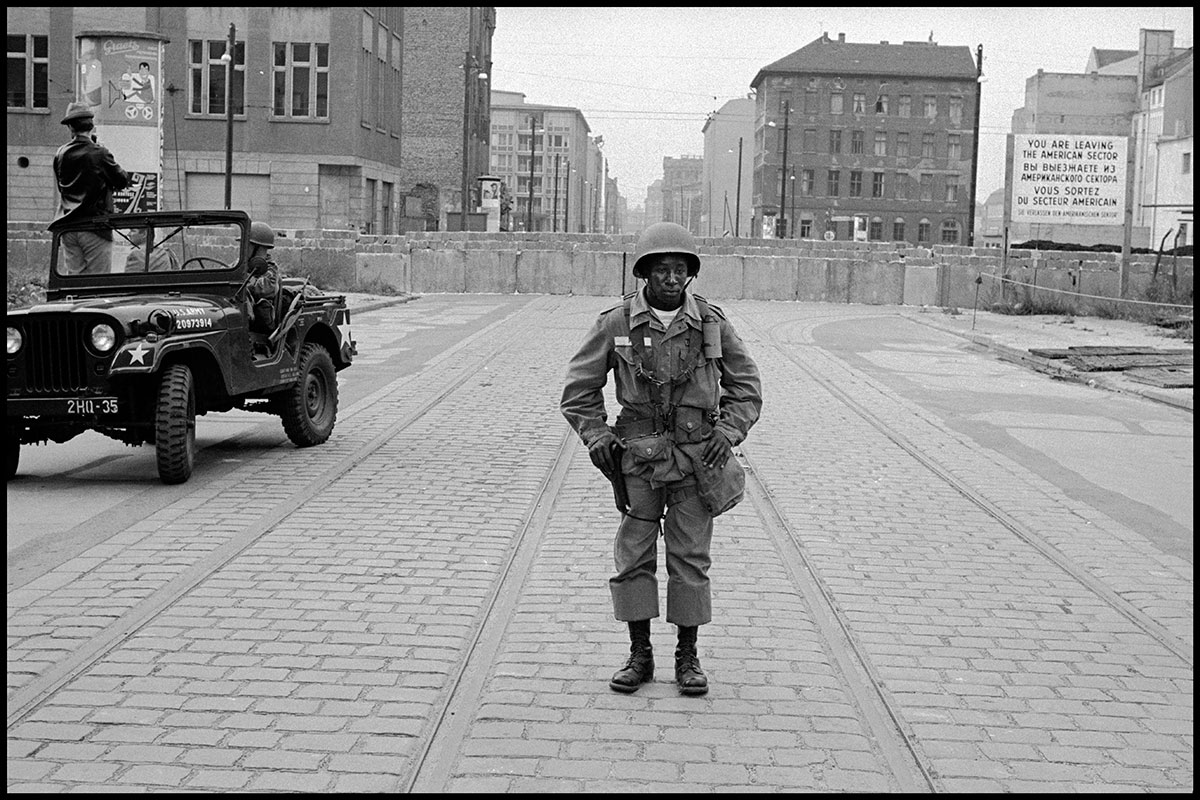 Photo of an American soldier standing with the Berlin Wall in the background