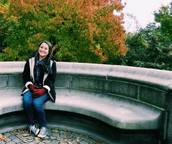 Kristen Andersen sitting on a stone bench in front of fall foliage