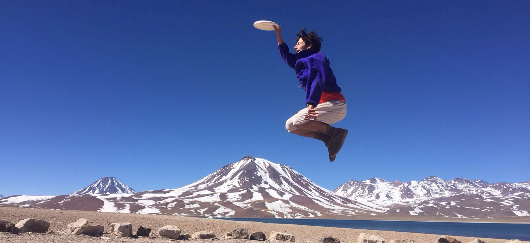 Student jumping in the air catching a frisbee with mountains behind him