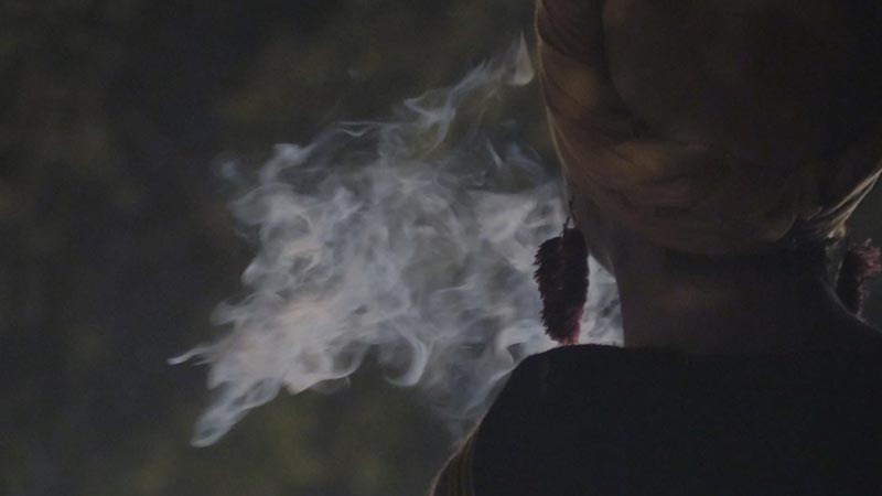 a woman viewed from behind as smoke billows out into the darkness
