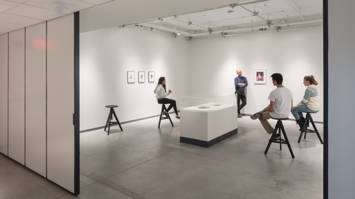 Students sit on stools in 006 Create Space and discuss what's on display