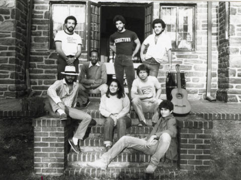 Black-and-white photograph of eight students standing and sitting on the brick steps outside of a house. steps outside 