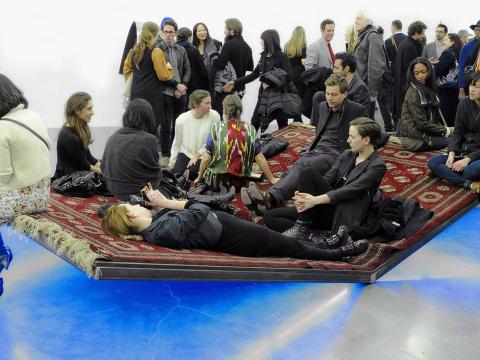 People sit on an angled carpet at an exhibition in New York