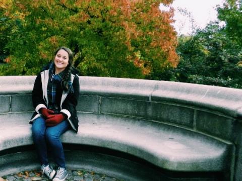 Kristen Andersen sitting on a stone bench in front of fall foliage