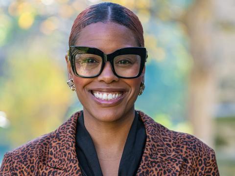 Ahyana King smiles, wearing very stylish glasses, outside on campus in the fall. 