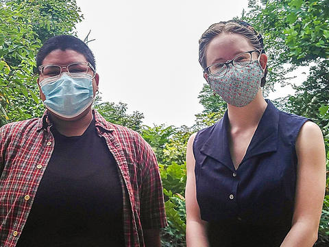 Alex on the left and Lily on the right wear masks and stand outside surrounded by trees