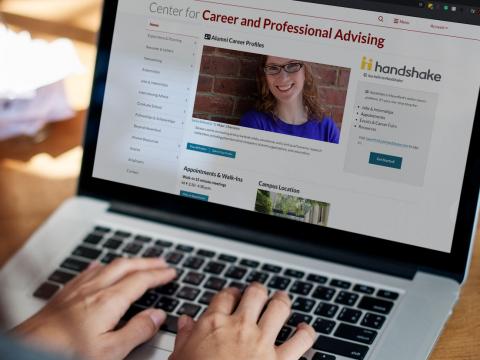 A laptop screen, viewed over the shoulder of an unseen student, showing the homepage for the Center for Career and Professional Advising