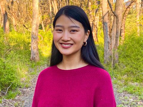 Claire Cai '21 smiles, wearing a pink sweater, on the Nature Trail. 