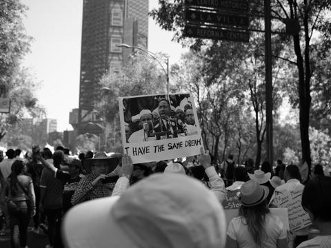 Person in crowd holds a sign aloft showing Marting Luther King Jr with the phrase I Have The Same Dream