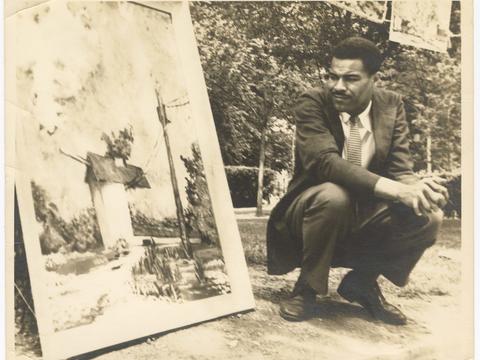 Paul B. Moses kneeling next to his painting The Ice House