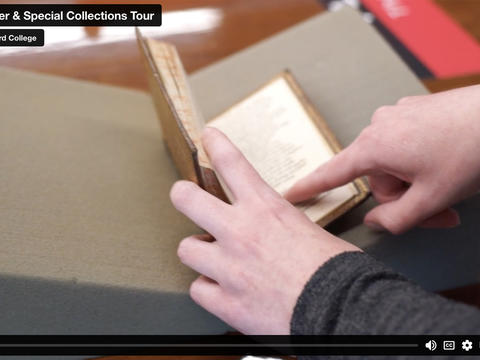 Video paused on two hands opening a small book and pointing inside