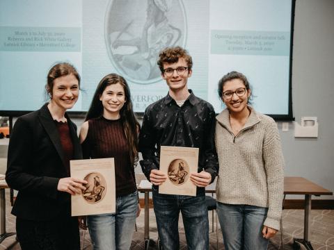 a photo of Sarah Watson and three student curators smiling and holding up the catalog of the Crossing Borders exhibit