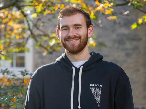 Zach Perry, wearing a black hooded sweatshirt that reads Oracle, stands in front of a building on Haverford's campus.