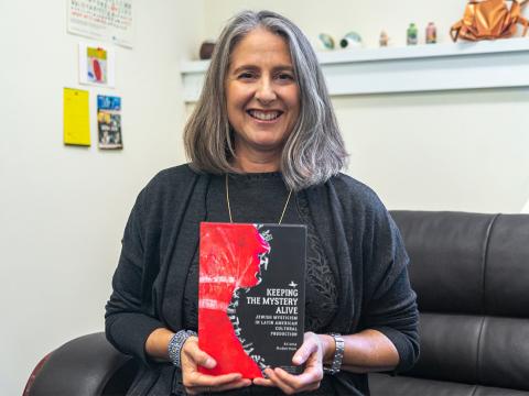 Photo of Spanish professor Ariana Huberman sitting and holding her new book, "Keeping the Mystery Alive: Jewish Mysticism in Latin American Cultural Production"