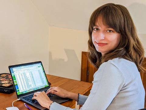 Laura Mercedes '24 sits at her desk in front of her computer, smiling.
