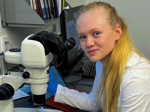 Rebecca Osbaldeston '24 sits in front of a microscope, wearing a lab coat.