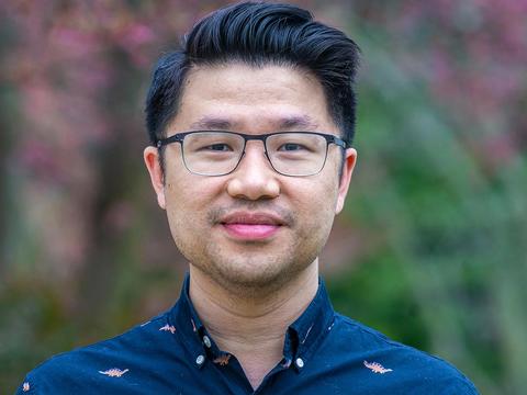 Standing against an out-of-focus background, Ryan Lei wears a blue shirt and glasses in a portrait taken on Haverford's camous.