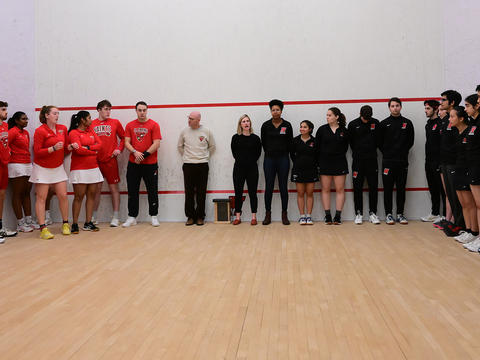 Members of the men's and women's squash teams line the walls of Haverford's court wearing the College's colors. 