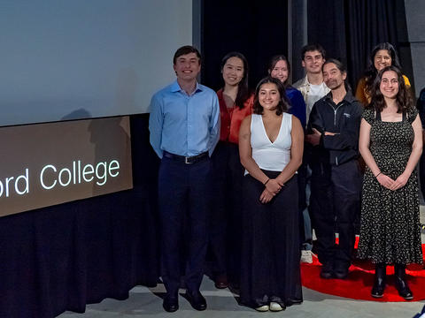 A group of 10, comprising Haverford students, staff and faculty, stand in front of a screen and a sign that reads TEDx Haverford College