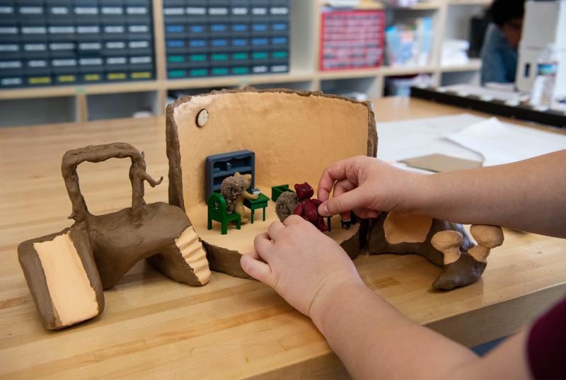 A hollowed-out tree trunk made of clay that's being used as a classroom for tiny clay squirrels