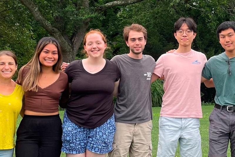 This summer's Charkoudian lab researchers, wearing shorts and t-shirts, stand in a line with their arms around each other. 