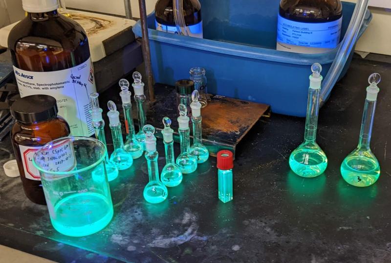 Glassware containing a solution of a molecule showing teal fluorescence