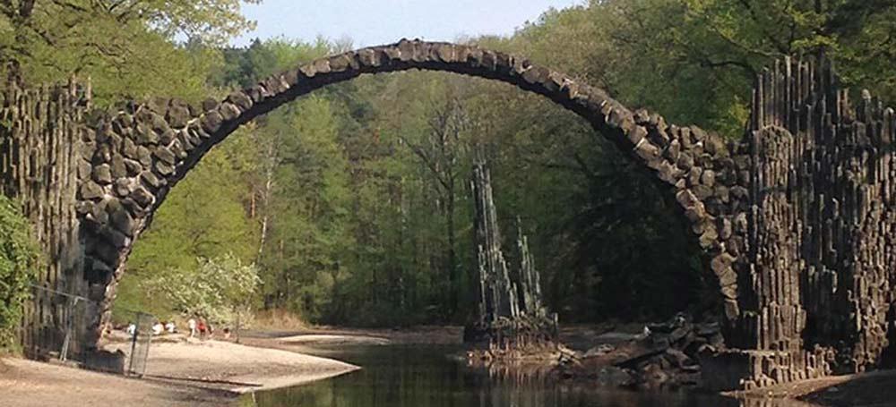 A jagged arched stone bridge and its reflection in the water, which forms an eerie circle