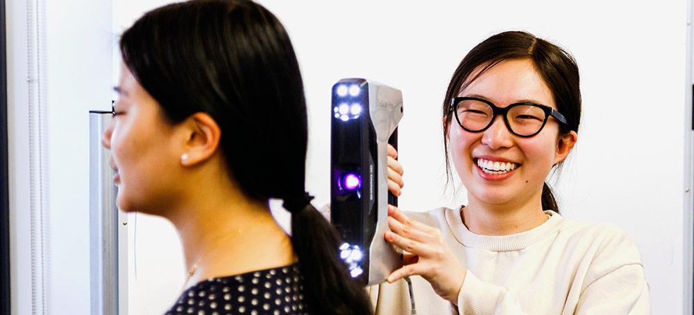 A student laughs while using a 3D scanner to scan her classmate