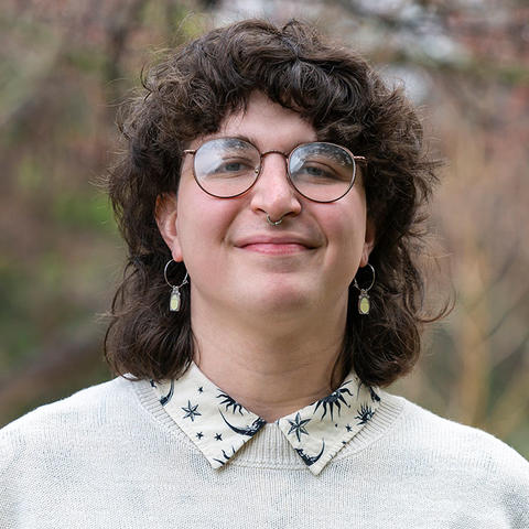 Headshot of June Scafiro, wearing glasses, earrings, and a white sweater with the collar of a white button down with navy blue astronomy print visible