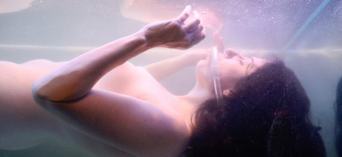 a naked women wearing a respirator suspended in a tank of water