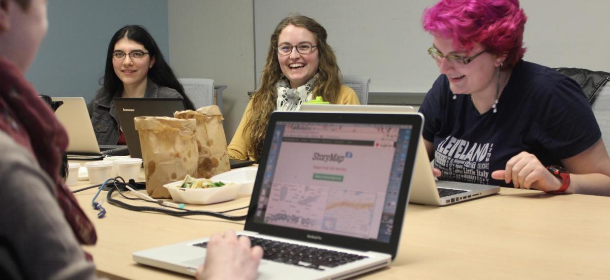 a group of student workers at a table, working at laptops and eating lunch