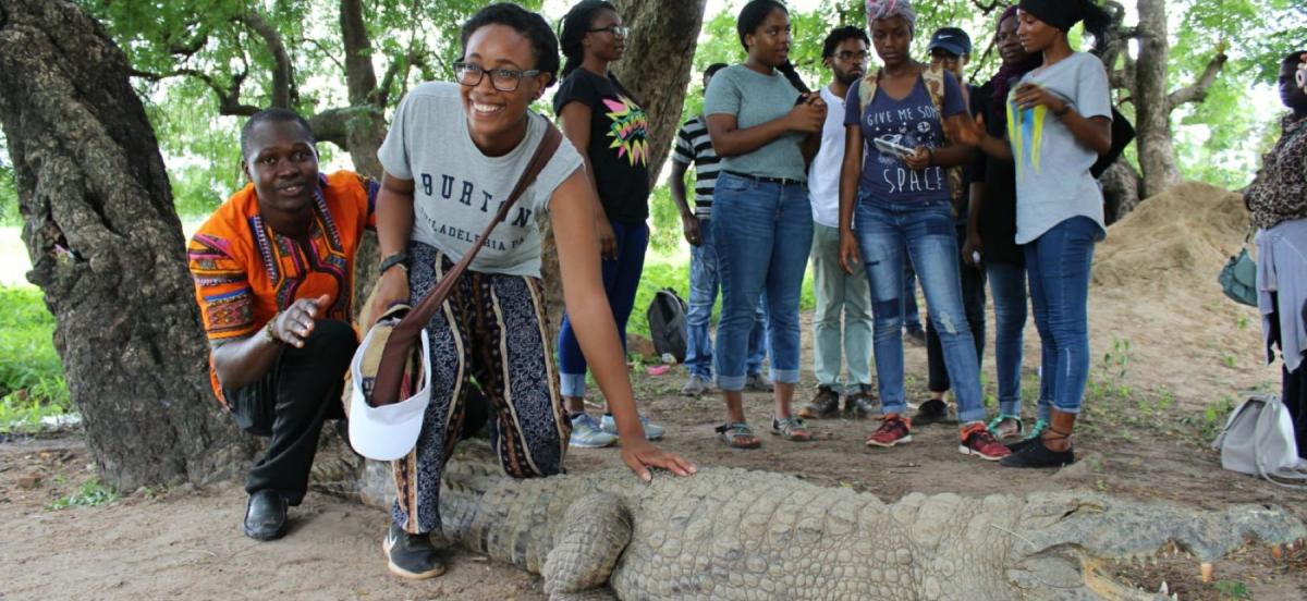 Woman leans over to pet an alligator in front of a group of people.