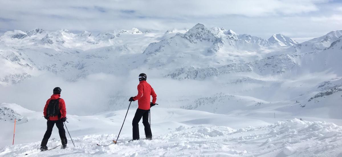 two skiers look out at large mountain covered in snow