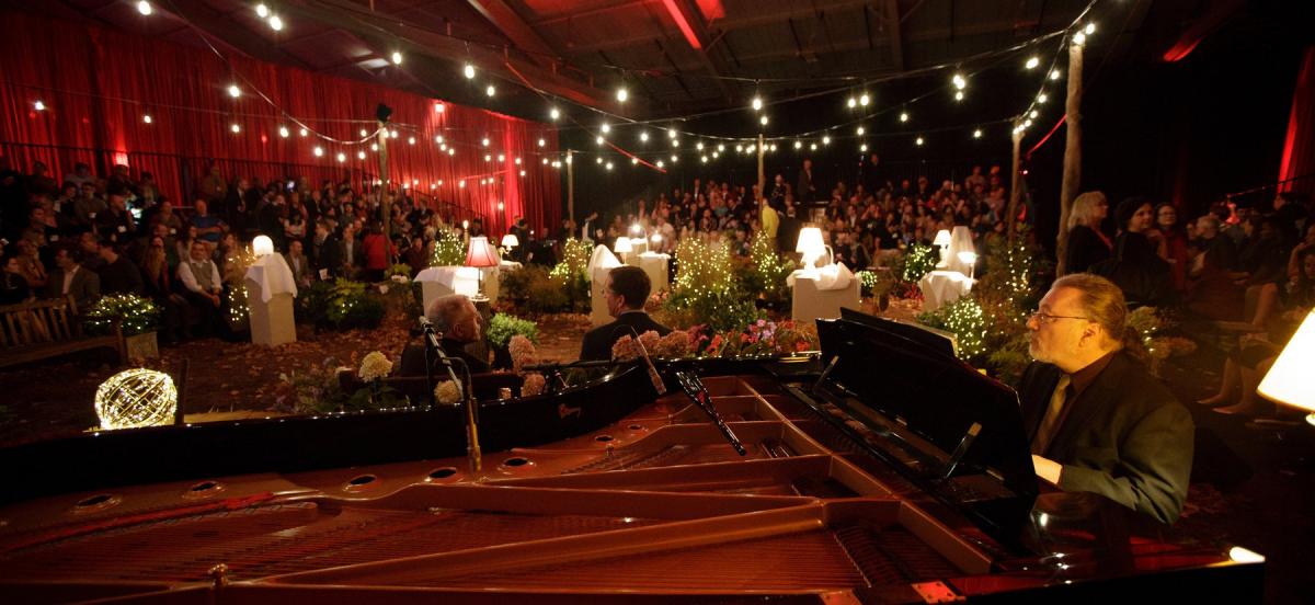 A man in the foreground plays piano in front of a celebration gala