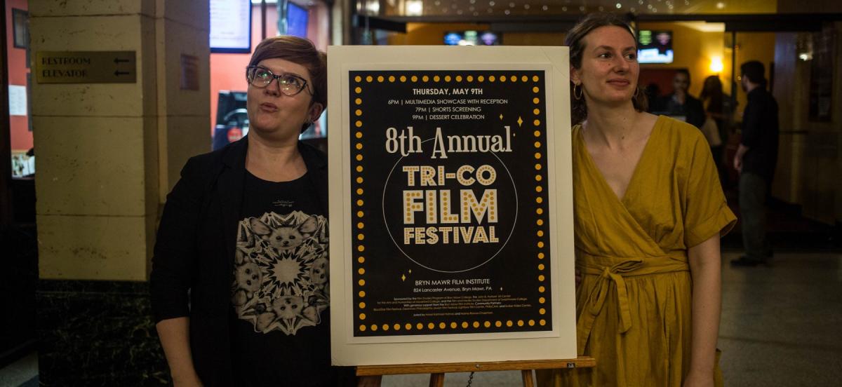 two women stand on either side of a sign promoting a film festival