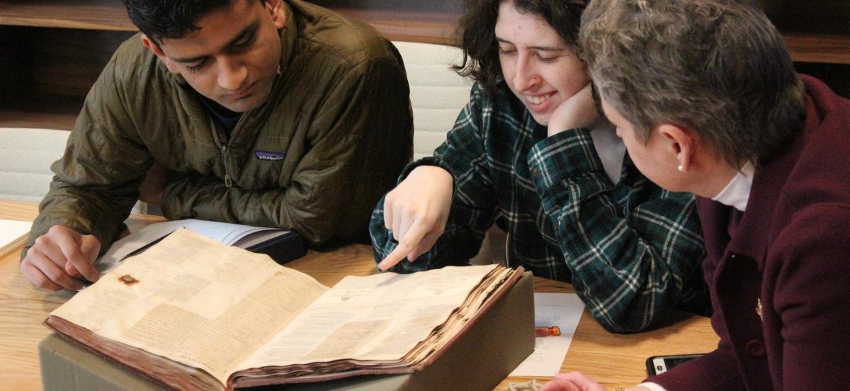 students and a faculty member looking at a rare book from Quaker and Special Collections