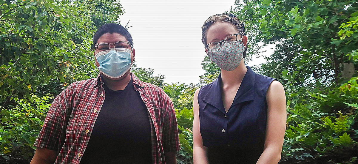 Alex on the left and Lily on the right wear masks and stand outside surrounded by trees