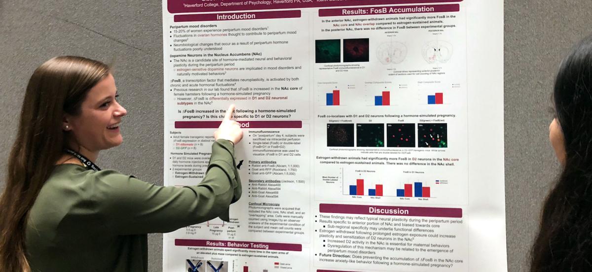 Alison Gibbons stands points at the neuroscience poster she co-authored