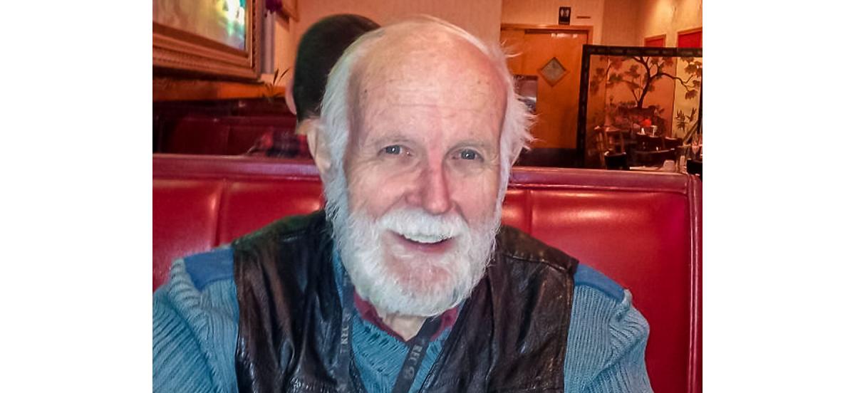Daniel Gillis smiles through his white beard while sitting in a red vinyl restaurant booth