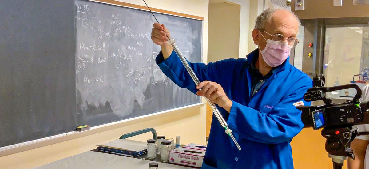 Instructor Mark Stein wears a mask while conducting a chemistry experiment for a video camera.
